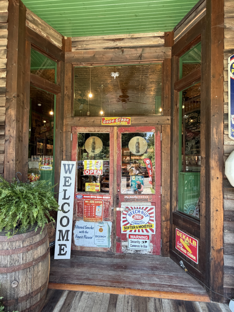 Rustic store entrance with wooden doors, 'Welcome' sign, and barrel planter.