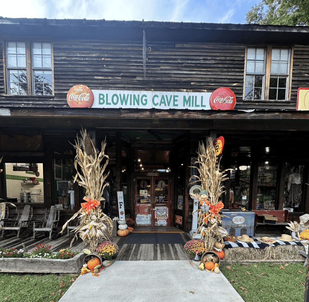 Rustic wooden store facade with fall decorations and Blowing Cave Mill sign.